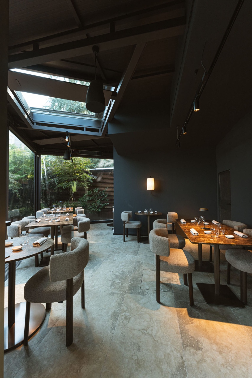 La sala di Miyama con vetrata sul giardino, poltroncine bouclé e tavoli in marmo